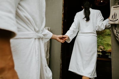 A couple holding hands in white robes walking into a private bathing pavilion