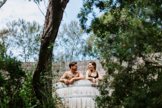 A man and woman in a barrel bath in the trees