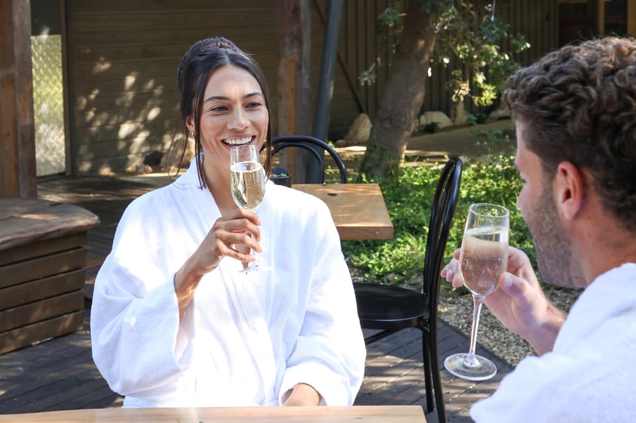 A woman in a white robe drinking a glass of sparkling wine