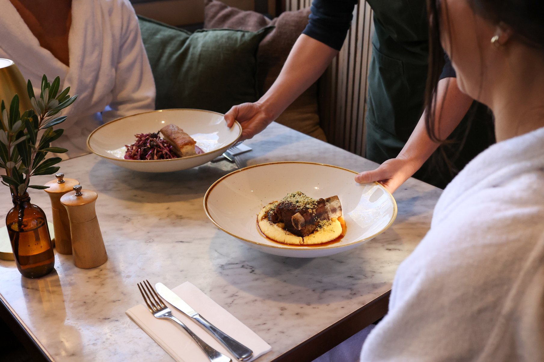 A waiter putting two plates of food on the table in the dining room